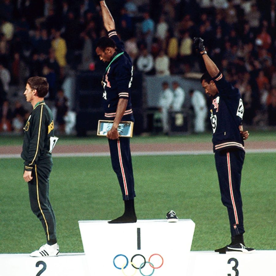African American runners Tommie Smith (center) and John Carlos (right) raise their firsts as the Star-Spangled Banner after their gold and bronze victories in the 200 m race at the 1968 Summer Olympics. Silver medalist Peter Norman (left) from Australia wears an OPHR badge in solidarity with their cause.